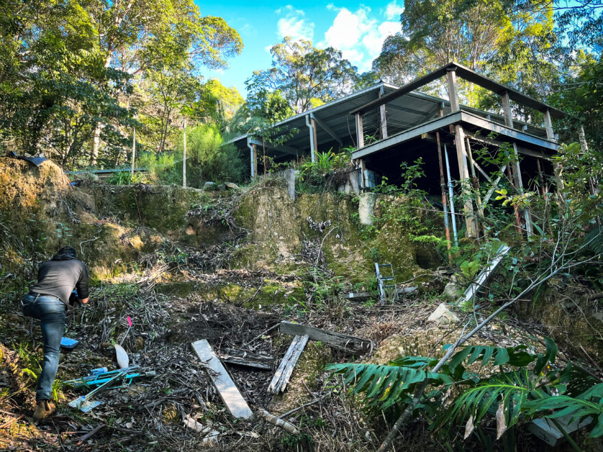 House affected by the Northern Rivers floods. There is metal and wood debris on the floor. A person is leaning over in the bottom left hand corner examining something.
